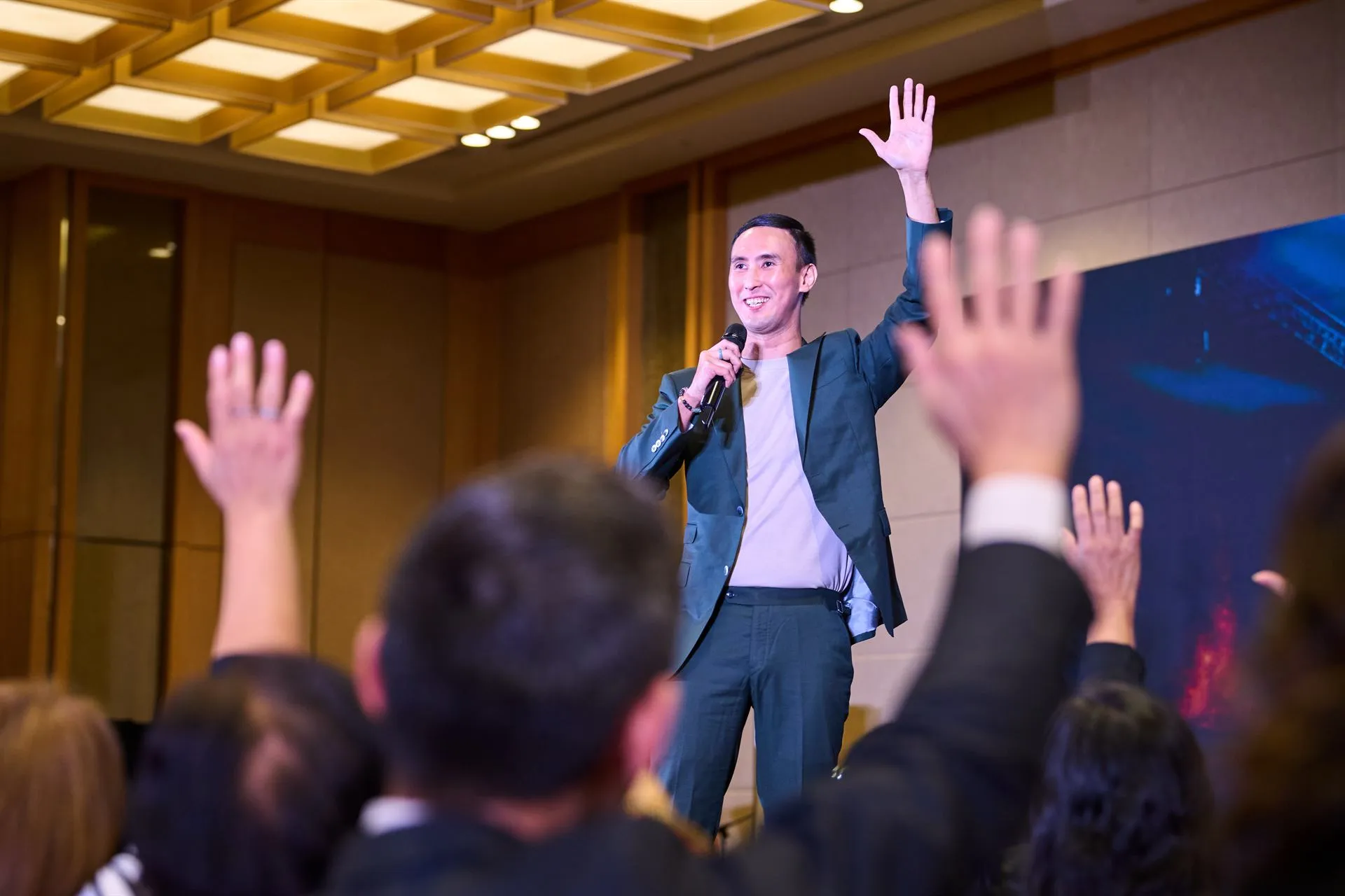 A packed audience raising their hands at an Envis8ge speaking event.
